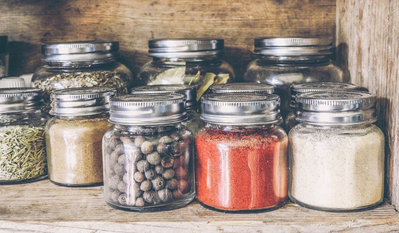 about-bg A collection of assorted spices in glass jars on a rustic wooden shelf for culinary use.
