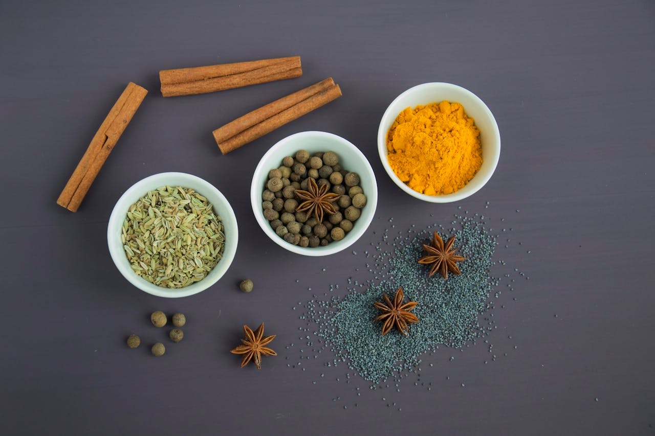 who-we-are Flat lay of assorted spices including cinnamon, turmeric, and star anise on a dark surface.